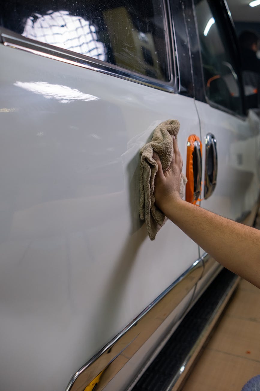 Hand gently wiping a car door with a microfiber cloth to remove a paint scuff